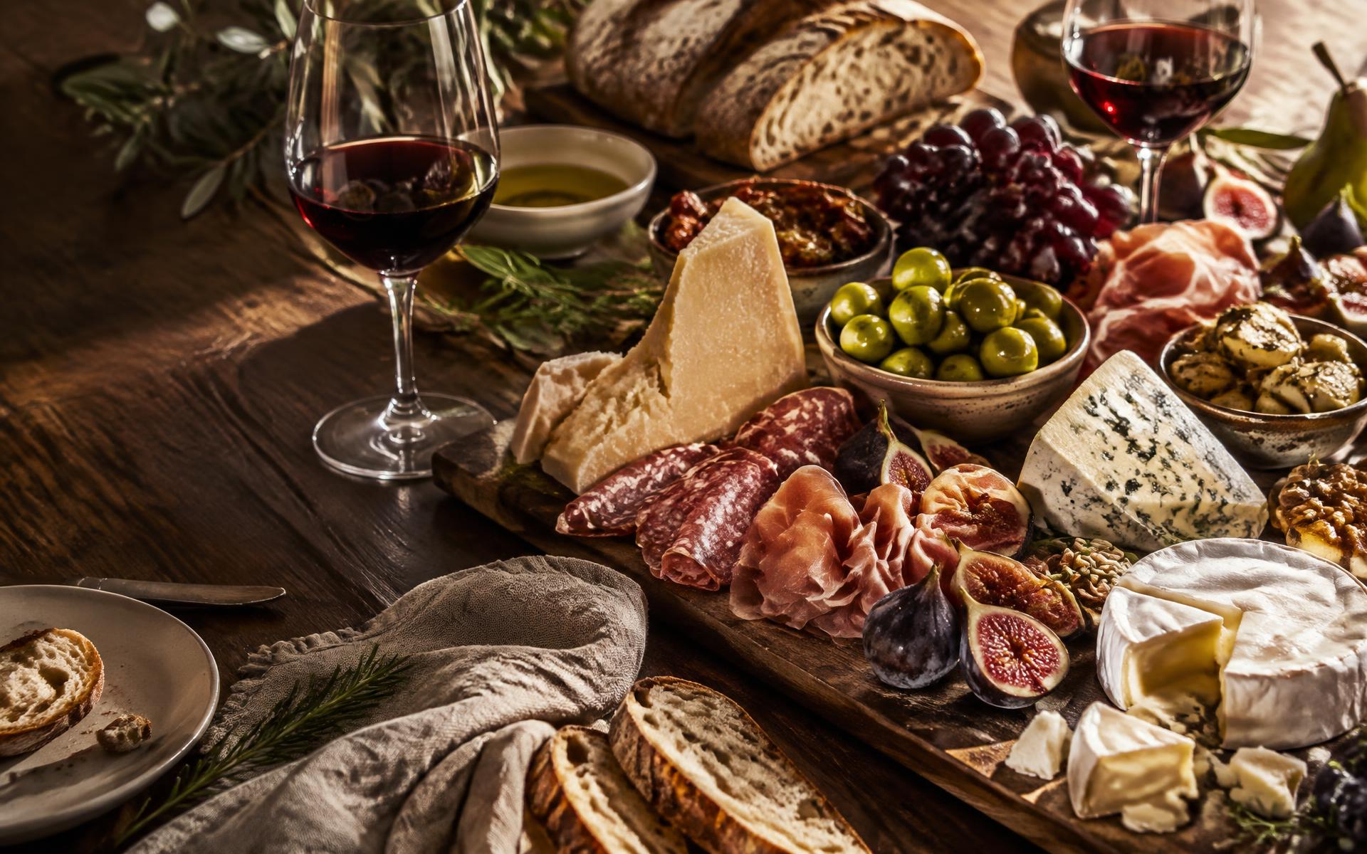 Mesa posta com queijos, frios, antepastos, frutas e vinho